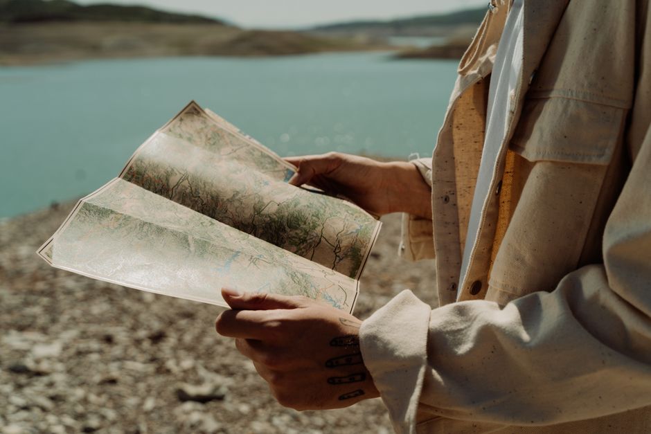 Person holding a map near a serene lake, embodying exploration and adventure.