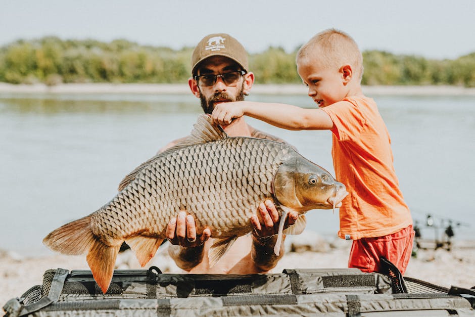 A man and a boy proudly display a carp caught by the lake on a sunny day.